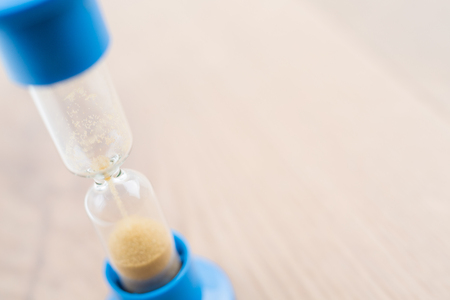 Closeup of blue hourglass on wooden desktop. Mock up