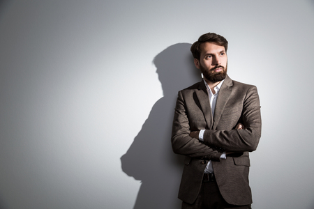 Bearded usinessman in suit standing against wall with shadow. Mock upの写真素材