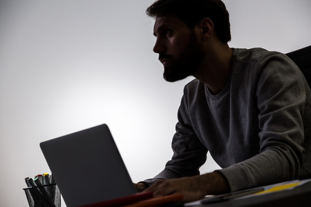 Silhouette of businessman working on notebook at office desk