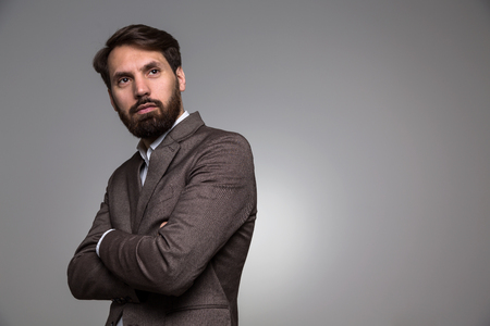 Businessman with crossed arms and beard  on grey background. Sideview, Mock upの写真素材