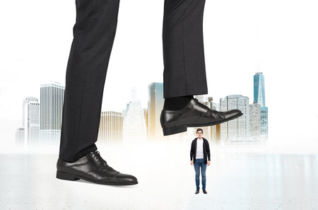 Abuse of authority concept with huge businessman foot stepping on a male miniature on New York city backgroundの写真素材