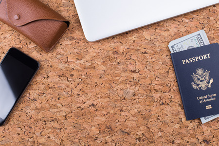 Topview of cork table with dollar banknotes inside american passport, smartphone and eyeglass case. Traveling concept. Mock upの写真素材
