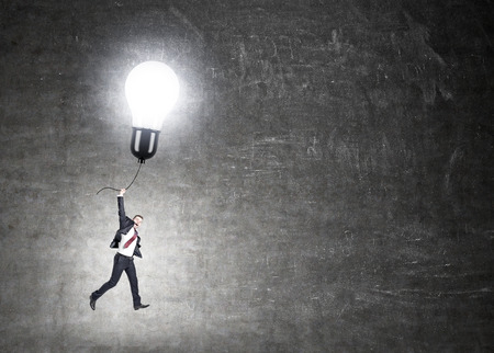 Idea concept with happy businessperson flying on illuminated lightbulb balloon on chalkboard backgroundの写真素材