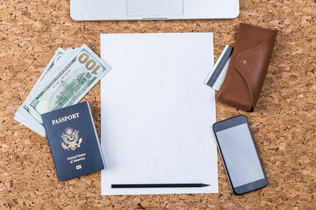 Top view of cork table with blank paper sheet, smartphone, eyeglass case, american passport and...