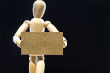 Wooden mannequin holding blank brown business card on black background. Mock upの写真素材