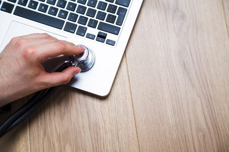 Closeup of hand listening to laptop with stethoscope on wooden desktop. Mock upの写真素材
