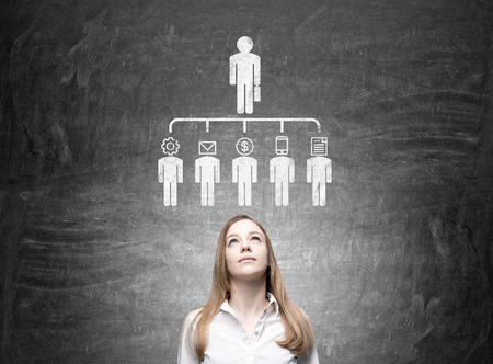Thoughtful businesswoman looking up at delegating pictogram sketch on chalkboardの写真素材