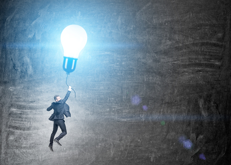 Idea concept with businessman flying on illuminated lightbulb balloon on chalkboard backgroundの写真素材