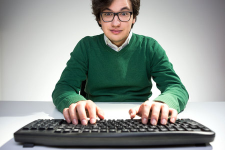Surprised young man with raised eyebrows using computer keyboard on white desktopの写真素材