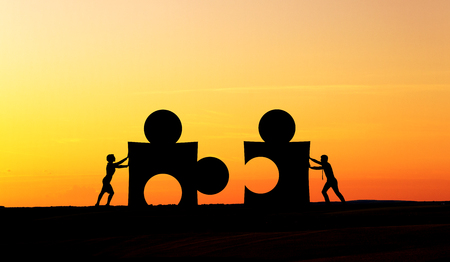 Partnership concept with businesspeople silhouettes putting puzzle pieces together at sunsetの写真素材