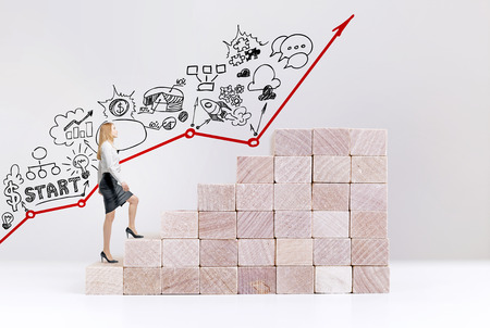 Businesswoman starting career path, climbing abstract wooden block stairs on white background with business sketch and arrowの写真素材