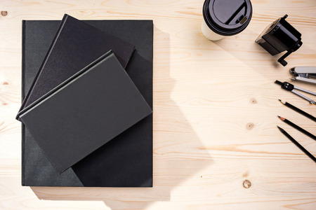 Top view of wooden desktop with closed notepads, coffee cup and stationery. Mock up