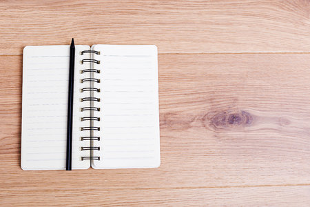 Top view of open spiral notepad and black pencil on wooden desktop. Mock upの写真素材