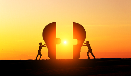 Businesspeople silhouettes putting lightbulb parts together at sunset. Concept of idea and partnershipの写真素材