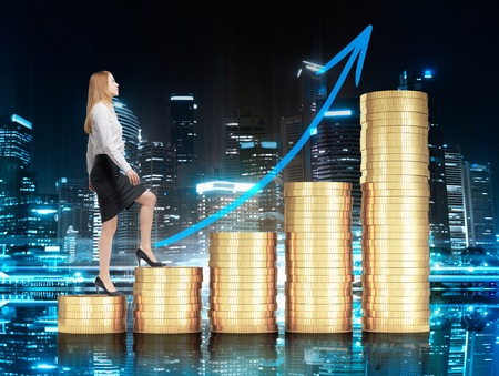 Financial growth concept with businesswoman walking up golden coin ladder with upward arrow on night city backgroundの写真素材
