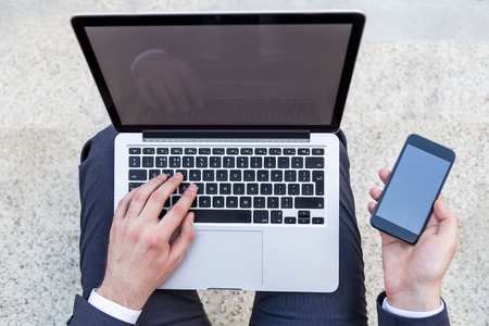 Top view of businessman with notebook on his lap and blank smartphone in hand. Mock upの写真素材