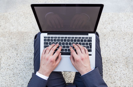 Top view of businessman typing on notebook keyboard placed on his lap. Mock up