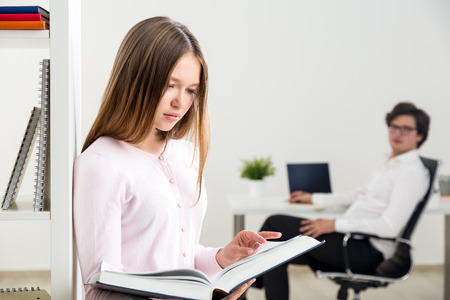Attractive businesswoman reading book in office and blurry businessman in the background looking at herの写真素材