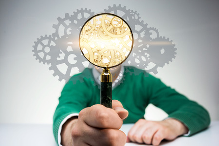 Search engine concept with man covering face with golden gear mechanism inside magnifierの写真素材
