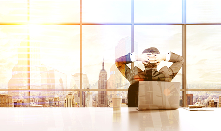 Back view of relaxing businessman on chair with hands behind head looking at New York city out of his office window. Double exposureの写真素材