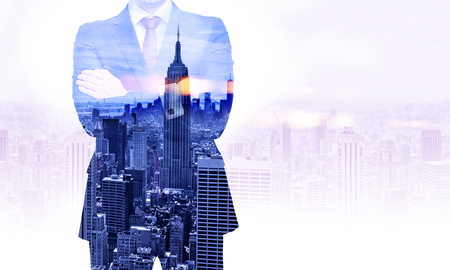 Front view of businessman with crossed arms on New York city background. Double exposureの写真素材