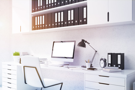 Closeup of office desktop with blank white computer monitor, coffee cup, plant, stationery items and shelves with documents above on concrete background. Toned image. Mock up, 3D Renderingの写真素材