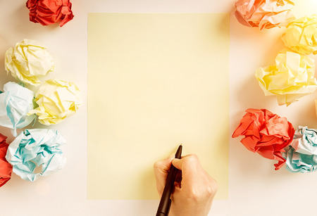 Hand drawing something on blank paper sheet surrounded with colorful crumpled paper balls. Mock upの写真素材