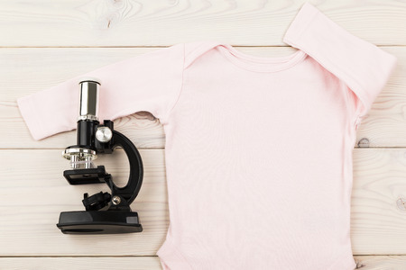 Future occupation concept. Pink baby girl outfit and microscope on light wooden surface. Closeup,...
