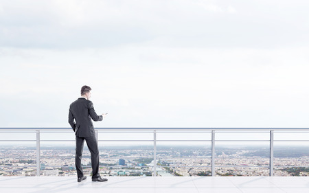Businessman using smartphone on city background with copy space. Back viewの写真素材
