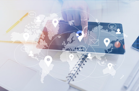 Businessman hand using tablet with network map on bright office desktop with objects. Social...