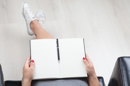 Girl in leather armchair sitting with her notebook and pen in her hands. Concept of creative work. Mock up. Top viewの写真素材