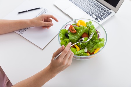 Woman eating her salad during lunch break at her desk in office. Bowl of colorful and healthy salad on table. Concept of enjoying good lifestyle. Top view.の写真素材
