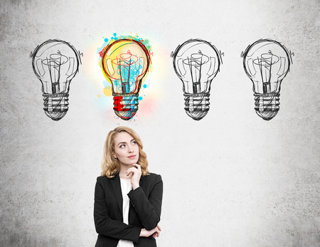Woman in suit standing near concrete wall with light bulb doodles and thinking. One out of four lbulbs is lit. Concept of high probabilityの写真素材