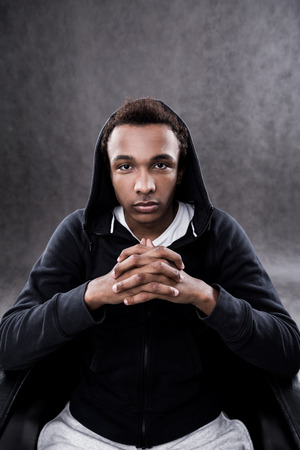 Serious African American man sitting in armchair with his fingers crossed. Concept of new beginningの写真素材