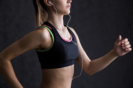 Close up of girl's torso. She is running in black sports bra with headphones and smartphone. Concept...