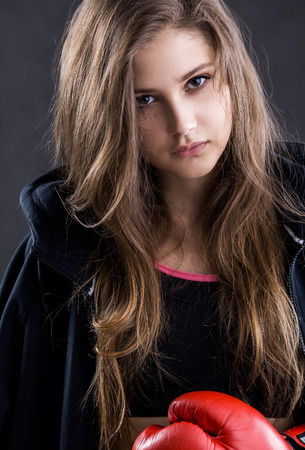 Serious girl with long hair in red and black boxing gloves looking to camera. Concept of professional sports.の写真素材