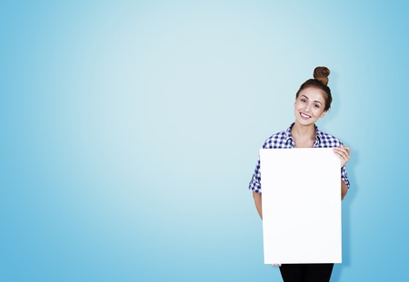 Girl in checkered shirt holding big vertical poster standing against blue background. Concept of advertising. Mockupの写真素材