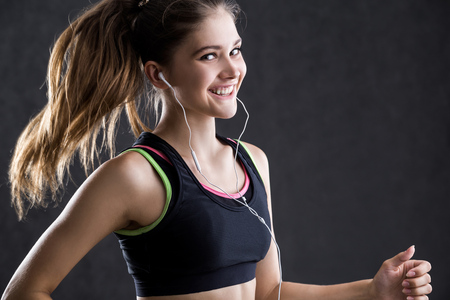 Close up of smiling girl in sport clothes with headphones against gray wall. Concept of healthy way of lifeの写真素材