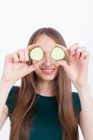 Girl with cucumber near eyes is smiling to camera. Concept of healthy and natural remedy. Mock upの写真素材