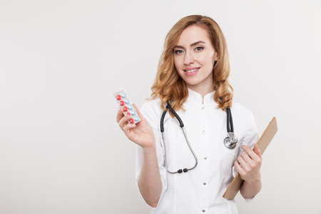 Smiling woman doctor standing with pills and clippad in her hands. Concept of right diagnosis. Mock upの写真素材