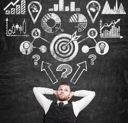 Businessman sitting near chalkboard with charts and start up sketch on it. Concept of new project launching.の写真素材