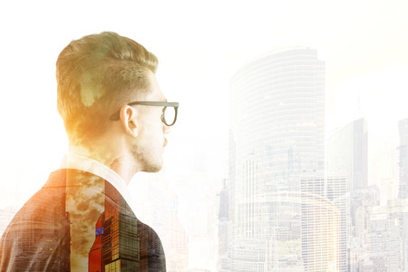 Portrait of businessman in glasses looking at big city skyscraper. Concept of large company employee.  Toned image. Double exposure.の写真素材