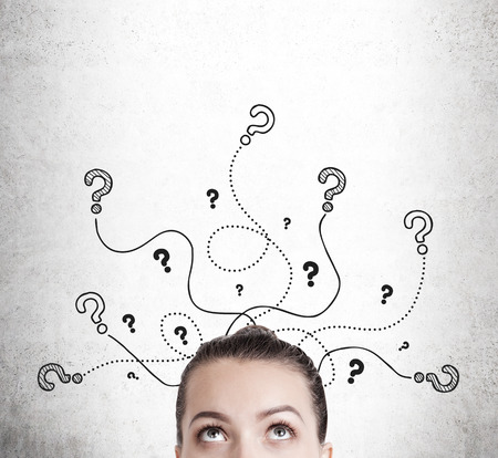 Close up of woman's head looking at question marks on concrete wall. Concept of searching for an answer. Mock upの写真素材