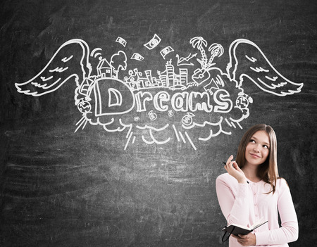 Portrait of girl with notebook dreaming about voyage. Blackboard with sketch at the background. Concept of tourismの写真素材