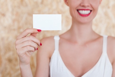 Smiling girl holding a blank business card in her hand with red nails. Concept of advertising an PR. Mock upの写真素材