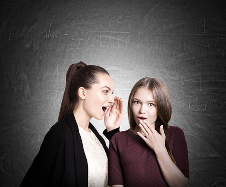 Two college students in casual clothes are gossiping near blackboard. Concept of rumor circulation. Mock upの写真素材