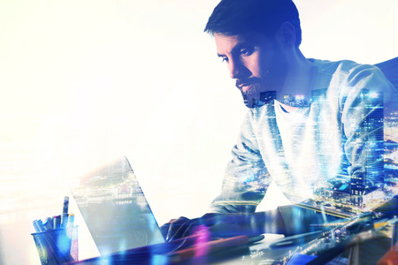 Side view of bearded caucasian businessman working on laptop at office desk with pencil glass  and...