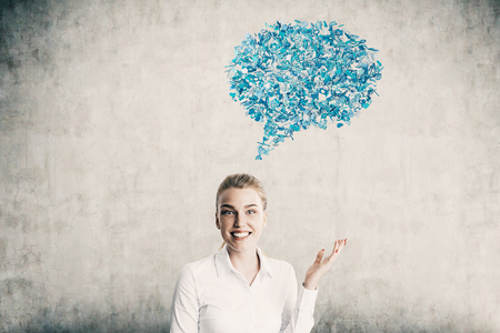 Cheerful blond girl standing near concrete wall with blue speech bubble. Concept of learning foreign languages. Mock up. Toned imageの写真素材