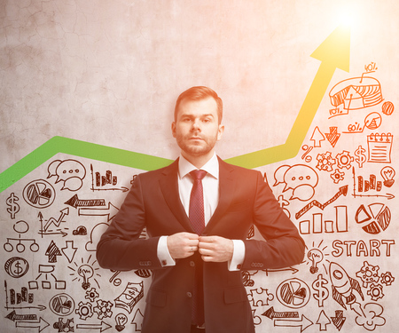 Serious man in red tie buttoning his vest near concrete wall with green graph and startup sketch. Mock upの写真素材