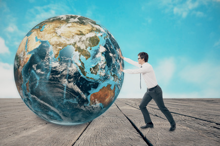 Side view of young businessman pushing the globe against sky themed wall and wooden floor. Concept of huge accomplishment. Mock up. Toned imageの写真素材